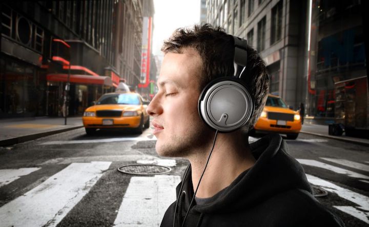 A man crossing a busy street with his eyes closed and wearing headphones.