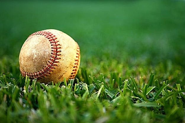 A worn baseball sitting in the grass.