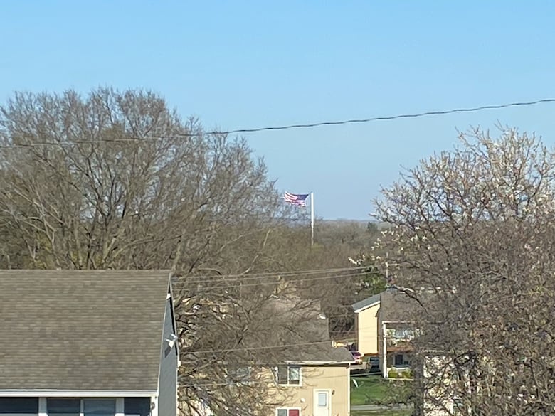 Photo shows a flagpole in the distance with anU.S. flag standing straight out from a strong wind.